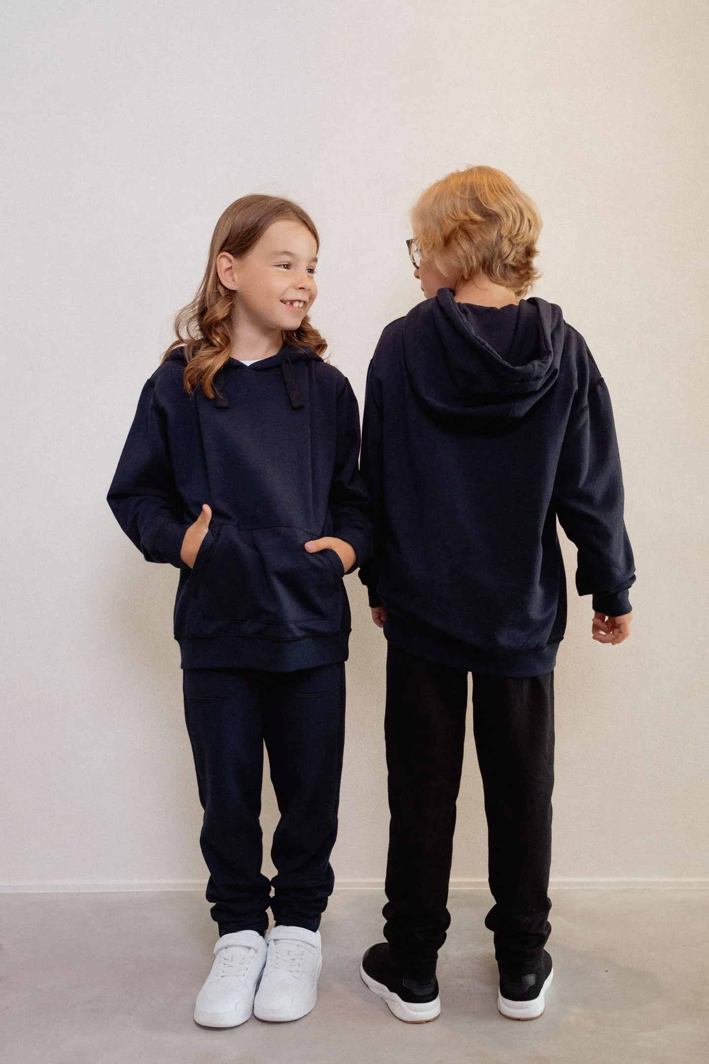 Twee kinderen dragen een marineblauwe fidget hoodie; ontspannen houding en zachte stof laten zien hoe comfortabel de fidget hoodie kind aanvoelt.